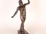 statue en bronze représentant un homme tenant une balle de tennis, posée sur un socle en bois