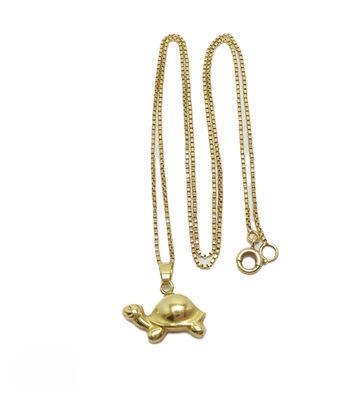 un gros plan d'un collier en forme de tortue dorée sur fond blanc