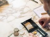 un homme assis à une table, avec un portefeuille et des pièces de monnaie devant lui