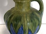 un vase vert et bleu posé sur une surface blanche