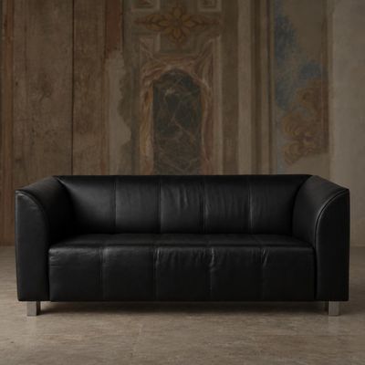 Le canapé en cuir noir se trouve devant un mur sur lequel est accroché un tableau.