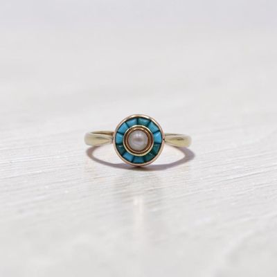 une image représentant une bague en or ornée d'une pierre turquoise et d'une pierre blanche au centre