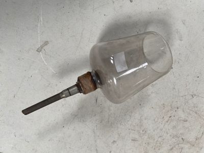 une bouteille en verre munie d'une poignée en bois, posée par terre