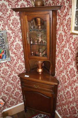 une armoire d'angle avec une porte vitrée, placée dans un coin de la pièce