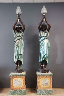two statues of women holding pots on their heads in front of a gray wall