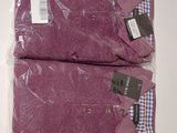 two purple shirts wrapped in plastic on top of a white table