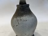 a gray vase with a black lid sitting on a white surface