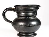 un vase noir muni d'une anse, posé sur une surface blanche