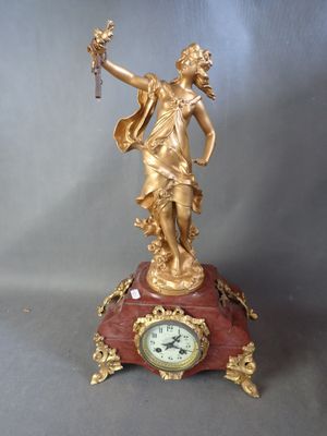 une statue en or représentant une femme tenant un oiseau sur une horloge rouge