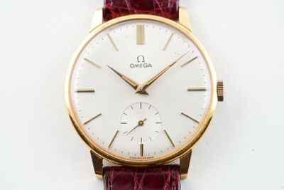 une montre en or avec un cadran blanc sur un bracelet rouge