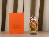 an orange box sitting next to a bottle of perfume on top of a wooden table