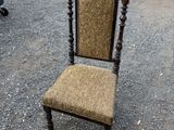 Une vieille chaise dont l'assise est recouverte d'un tissu marron se trouve sur un parking