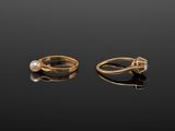 two gold rings with pearls and diamonds on a black surface