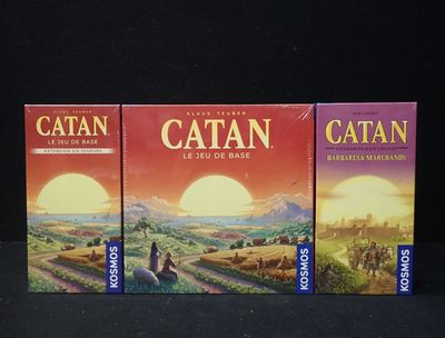 trois boîtes du jeu Catan posées sur une surface noire