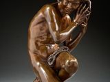 une statue en bronze représentant un homme à genoux, les mains sur le visage