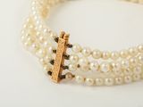 three strands of white pearls with a gold clasp on a white surface