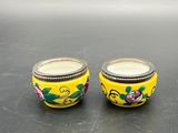 pair of yellow glass jars with floral designs on them sitting on a table