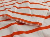 an orange and white striped fabric on a bed with white sheets