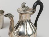 two silver teapots and a silver cup on a white surface