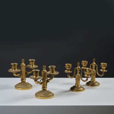 three brass candelabs on a white table with a black background