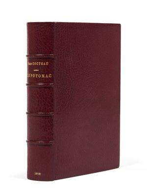 un livre rouge avec des lettres dorées posé sur une surface blanche