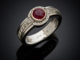 a close up of a ring with a ruby stone and diamonds
