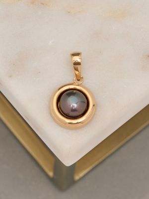an image of a gold pendant with a black pearl on a marble surface