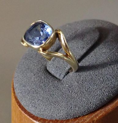 une bague ornée d'une pierre bleue, posée sur un socle en bois