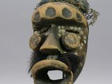 une image représentant un masque en bois posé sur un socle en métal