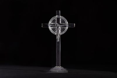 a clear glass cross on a black surface with a black background