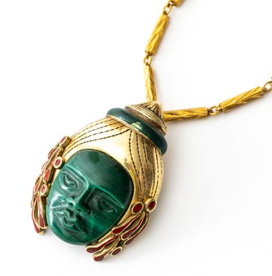 une image représentant un collier vert et doré orné d'un visage