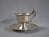 a silver cup and saucer sitting on a saucer