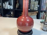 un vase rouge posé sur une table devant une bibliothèque