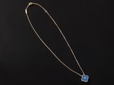 a gold necklace with a blue flower pendant on a black background