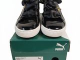 des baskets Puma noires et blanches ornées de nœuds, posées sur une boîte verte