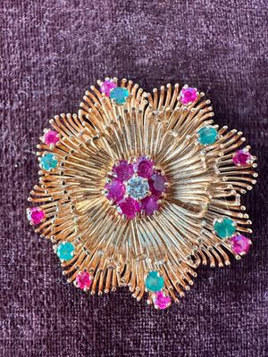 une image représentant une broche en or sertie de pierres roses, vertes et bleues