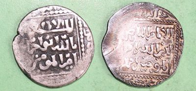 two silver coins with arabic writing on them on a green surface