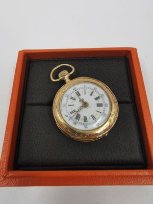une montre de poche en or dans un écrin, posée sur une surface blanche