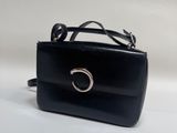 Le petit sac à main noir est muni d'un anneau métallique sur la poignée.