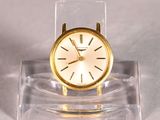 a small gold clock on a clear stand on a white surface