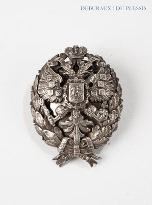 une broche en argent sur laquelle figurent des armoiries et une couronne