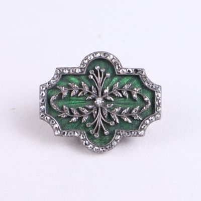 a close up of a green and silver broochle on a white surface