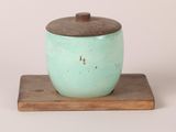 un petit pot vert muni d'un couvercle en bois, posé sur un socle en bois