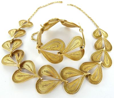 une photo représentant un ensemble composé d'un collier et d'un bracelet en or, posé sur un fond blanc