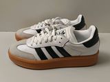baskets adidas blanches et noires avec des semelles en caoutchouc sur une base blanche
