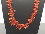 a necklace made of orange coral beads on a black display stand