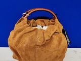 Sac à main marron à poignées tressées posé sur une table blanche devant un mur bleu