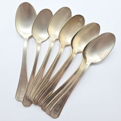 six cuillères en argent sont disposées en ligne sur une surface blanche