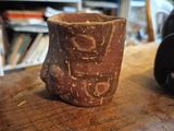 a brown cup sitting on a wooden table next to a camera