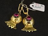 deux boucles d'oreilles en or ornées de pierres roses, posées sur un fond noir